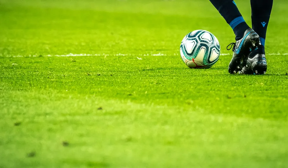Balón y pie de un futbolista sobre césped. Fotografía ilustrativa.